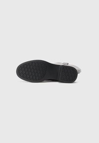 Semelle en caoutchouc noir avec un motif de grip texturé, tige grise avec une finition lisse et un détail de sangle. Conçu pour la durabilité et l'adhérence.