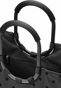 Bolso de tela negro con grandes lunares, con asas de textura negra y un bolsillo interior con cremallera. Material suave y forma redondeada.