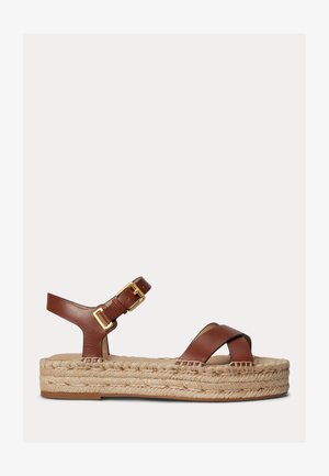 Hnedá kožená sandála s prekríženými remienkami, prackou na členku a hrubou pletenou platformou z juta na jednoduchom svetlom pozadí.