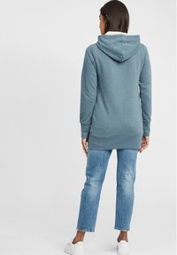 Sudadera con capucha de color azul claro, con una textura suave, un bolsillo tipo canguro y puños de canalé. Combinada con jeans rectos de color azul claro y zapatillas blancas.