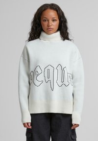 Weißer Rollkragenpullover mit geripptem Saum und Bündchen. Mit schwarzem, stilisiertem Text über der Brust. Weicher Stoff, entspannter Schnitt.