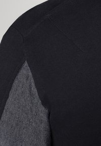 Maglietta nera in maglia con un pannello in denim grigio texturizzato sulla spalla. Presenta una finitura in tessuto liscia e una vestibilità su misura.