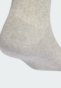 Světlounce šedá ponožka s texturovaným pleteným vzorem. Má hladký lem a zesílenou patu, představující měkkou tkaninu a bezešvý design.