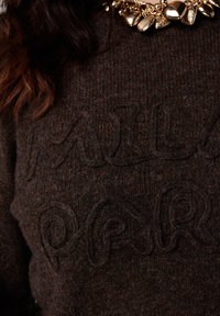 Bruine wollen trui met reliëftekst "MILAN PARIS". Gestructureerd gebreid patroon met een ronde halslijn en een dikke ketting in goudkleur.