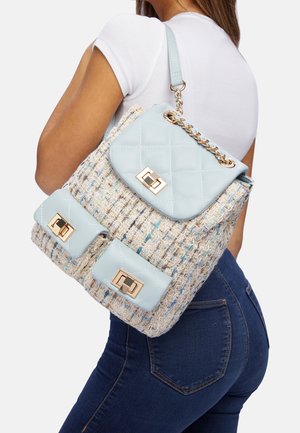 Sac à dos en simili cuir bleu clair matelassé avec un corps beige tissé, accents en matériel doré, deux poches avant et détails de chaîne.