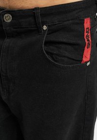 Schwarze Jeans aus Denim mit schmalem Schnitt, rotem Akzentlabel und Metallknöpfen, im klassischen Fünf-Taschen-Design.