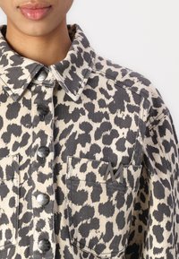 Giacca di jeans a fantasia leopardata in beige e nero con bottoni metallici, taschino sul petto con logo impresso e colletto classico.