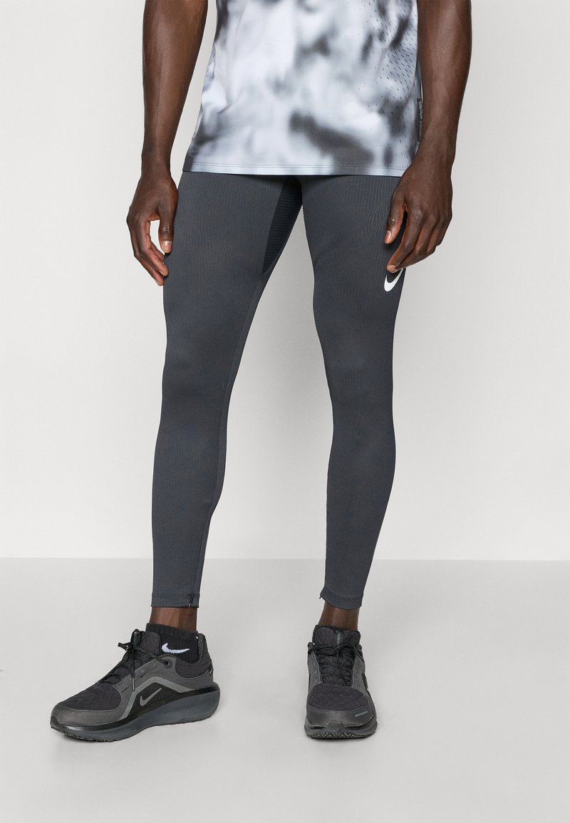 Graue Sportleggings mit gerippter Textur und figurbetontem Design, kombiniert mit schwarz-grauen Laufschuhen mit einem weißen Logo.