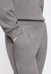 Šedé tepláky vyrobené z měkkého materiálu, se boční kapsou a pohodlným pasem, s jednoduchým a elegantním designem.