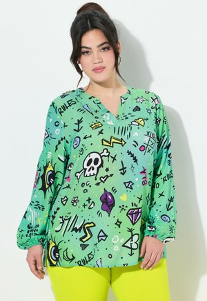 Blouse verte à manches longues avec un décolleté en V, ornée d'un imprimé graphique ludique de symboles et de griffonnages en noir, jaune et rose. Tissu lisse.