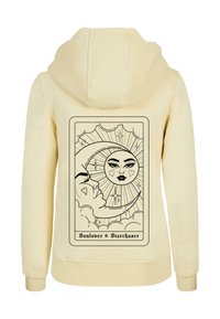 Krämfärgad huvtröja med en grafisk tryck av en sol och måne med hjärtan. Designen är omgiven av svart, mot den mjuka tyget.