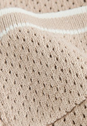 Tissu tricoté en beige clair avec un motif texturé, présentant des trous ajourés et une bande blanche contrastante le long d'un bord.