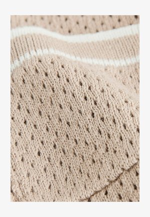Pletena tkanina v svetli bež barvi z teksturiranim vzorcem, ki vsebuje odprte luknje in kontrastno belo črto ob robu.