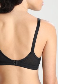 Svart BH med mesh-design, tynne stropper og lukking bak. Har glatt tekstur og subtile sømdetaljer.