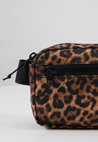 Sac banane en tissu imprimé léopard avec poche avant zippée et sangle noire réglable sur un fond neutre.