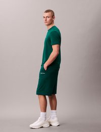 T-shirt en coton vert et shorts assortis, avec le logo Calvin Klein, coupe décontractée, associés à des baskets blanches et des chaussettes mi-hautes.