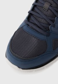 Close-up of a navy blue athletic shoe with mesh fabric, synthetic overlays, navy laces, and a white rubber sole.