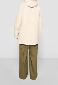 Veste matelassée couleur crème avec capuche, associée à un pantalon cargo vert olive avec de grandes poches latérales et une coupe à jambes larges.