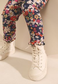 Blå leggings med blommönster, ribbad textur och volangkant, kombinerade med vita höga sneakers med snörning och gummisula.