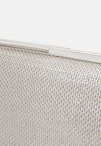 Pochette de soirée en maille argentée avec un cadre et un fermoir métaliques, présentée en gros plan sur un fond blanc.