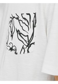 Hvid t-shirt med korte ærmer, forsynet med en sort blomstret lappelomme på venstre side. Blødt, let stof.