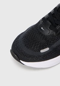 Czarne, dzianinowe buty sportowe z teksturowaną górą, gładkimi czarnymi akcentami i białą podeszwą. Zawierają wentylację i detale logo.