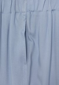 Ljusblått tyg med en mjuk textur och subtil diagonal väv, med ett midjeband med elastisk samling och sidofickdetalj.