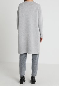 Dlouhý šedý pruhovaný pletený svetr s kulatým výstřihem, spojený s lehce šedými texturovanými džíny a černými kotníkovými botami.