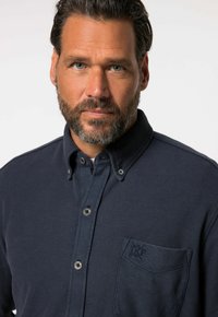 Camicia blu navy con bottoni realizzata in tessuto testurizzato, dotata di tasca con dettagli ricamati e bottoni a contrasto.