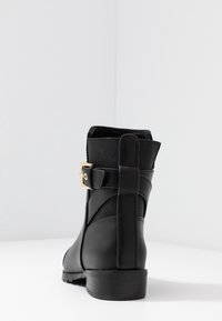 Schwarze Knöchelstiefel aus glattem Leder mit einem strukturierten Stoffeinsatz. Mit einem goldenen Schnallen-Detail und einem niedrigen, klobigen Absatz.