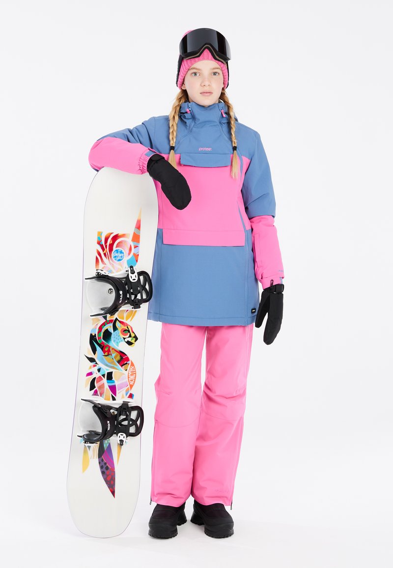 Snowboarder con un traje azul y rosa, sosteniendo una tabla de snowboard con gráficos coloridos. Incluye un cuello alto, manoplas y gafas de esquí.