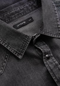 Donkergrijze denim overhemd met een spitse kraag, zwarte knopen en een binnenlabel met "ombre" en maat "M32." Rijke textuur en gestructureerd ontwerp.