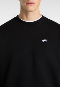 Felpa nera con scollo rotondo e polsini a costine. Presenta una piccola grafica di uno skateboard ricamata in bianco sul petto.