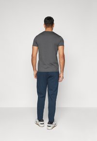 Gray short-sleeve t-shirt paired with blue sweatpants, featuring a relaxed fit and smooth texture. Shoes are white with black accents.