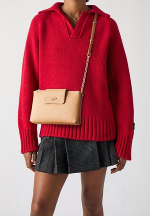 Czerwony sweter z dzianiny z kołnierzem, prążkowanym wykończeniem, zestawiony z plisowaną spódnicą w kratę. Beżowa torebka na ramię z klapką i łańcuszkiem.