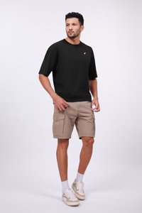 T-shirt noir à manches courtes avec un logo jaune, associé à un short cargo beige clair avec des poches latérales, porté avec des baskets blanches et beiges.