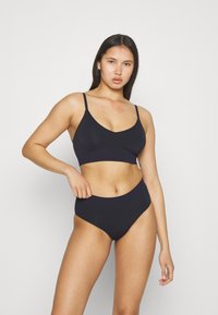 Zwarte naadloze bralette met verstelbare bandjes en bijpassende high-waisted slips. Zachte, rekbare stof met een gladde textuur.