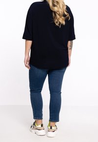 Mørkeblå oversized top med opslået korte ærmer, parret med tætsiddende blå jeans og hvide sneakers med neonlys og sort hardware.