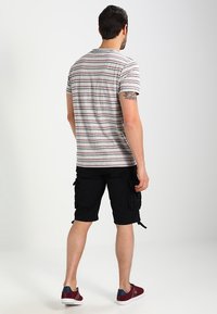 Šedé pruhované tričko s krátkým rukávem v kombinaci s černými cargo šortkami. Vzato s červenými a šedými botami. Viditelné tetování na paži.