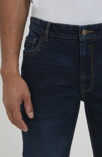 Tamno plave traperice od denima s klasičnim krojem, dizajnom od pet džepova, kontrastnim šavovima i zatvaranjem na jedan gumb u struku.
