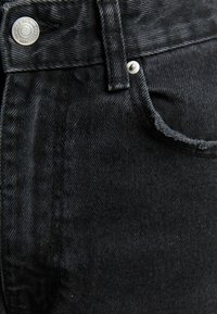 Svarta denimjeans med en närbild av tygets textur, knappdetaljer och distinkta sömmar vid fickområdet.