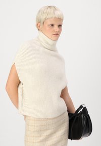 Off-white pletena turtlenecks s kratkimi rokavi, v kombinaciji z bež teksturirano krilo in majhno črno torbico z nabranim oblikovanjem.