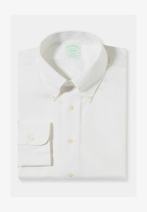 Bílá úzká košile s dlouhým rukávem, límečkem na knoflíky a knoflíky na manžetách, pečlivě složená na jednobarevném pozadí.