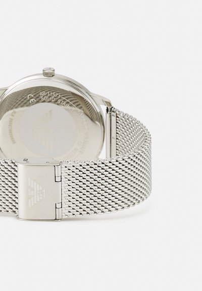 Silberne Edelstahl-Uhr mit einem Netzarmband. Verfügt über ein rundes Gehäuse, glatte Oberfläche und einen gebrandeten Verschluss. Transparentes Gehäuse auf der Rückseite zeigt das Innenleben.