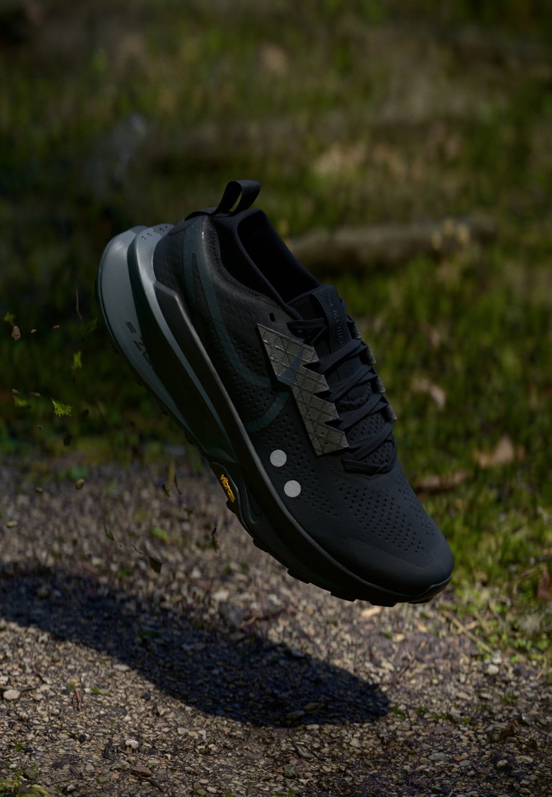 Black running shoe featuring a breathable mesh upper, a textured silver design element, and a chunky midsole with Vibram outsole.