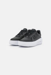 Black leather sneakers with textured panels, flat laces, and a white rubber sole. Features a raised logo on the tongue and side.