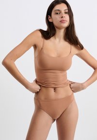 Brązowy dwuczęściowy strój kąpielowy wykonany z gładkiego, elastycznego materiału; z dopasowaną bluzką na ramiączkach i wysokimi majtkami bikini.
