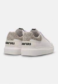 White sneakers with a textured gray heel, purple accents, and a chunky white sole. Features a black brand logo on the heel tab.