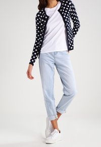 Navy polka dot cardigan over a white t-shirt, paired with light blue rolled-up jeans and white sneakers.