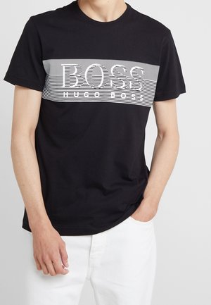 T-shirt en coton noir avec un motif rayé horizontal blanc arborant le texte "BOSS" et "HUGO BOSS" en lettres grasses et contrastées. Manches courtes.